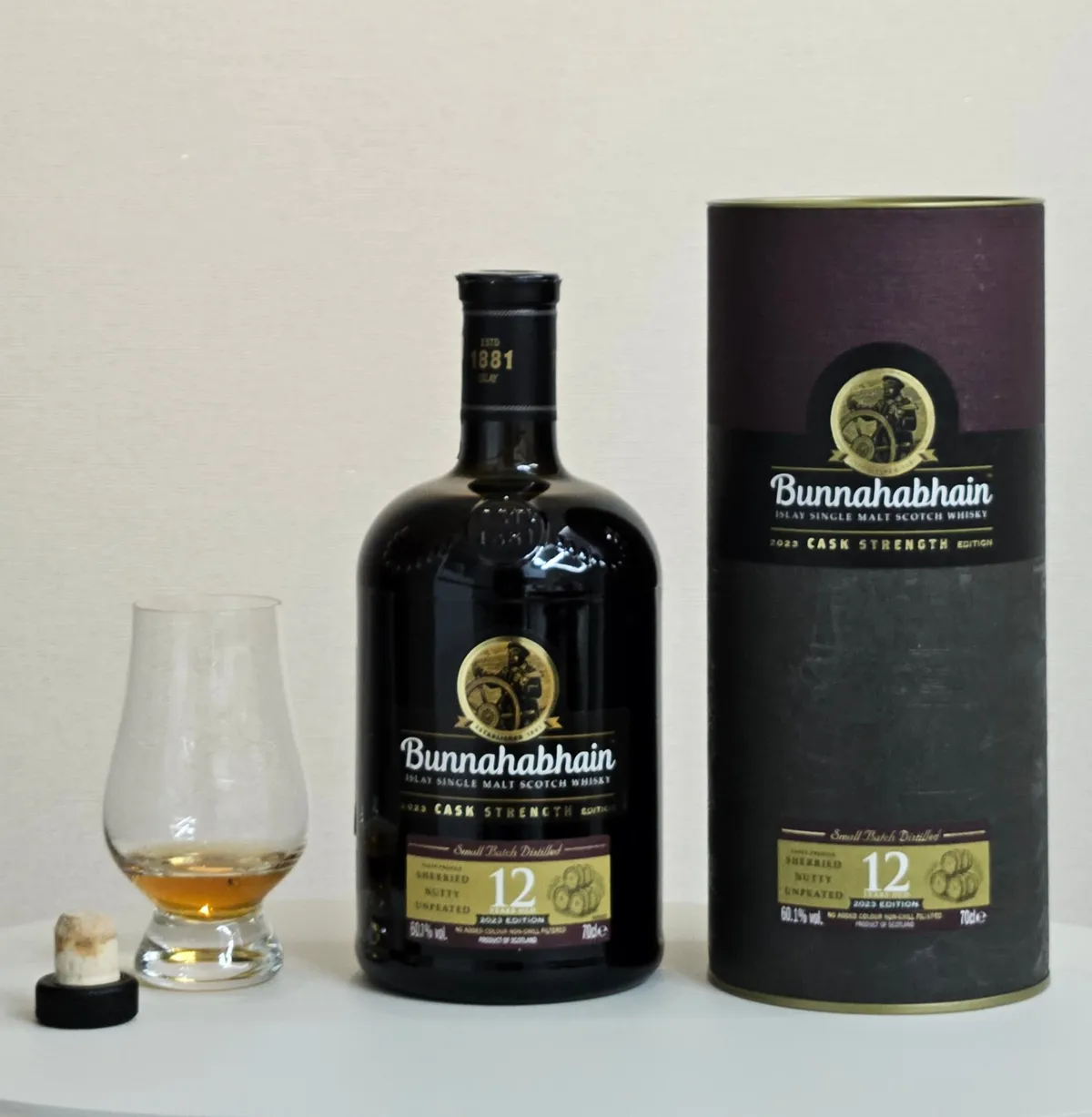 A bottle and tube of Bunnahabhain 12 Year Old Cask Strength 2023 Edition beside a Glencairn glass of whisky and the cork stopper
